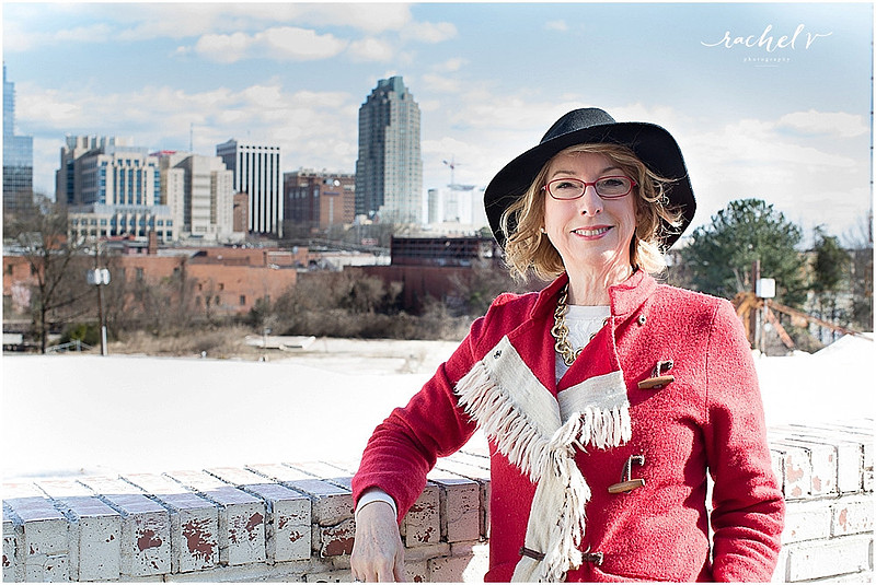 Couple standing by brick wall wearing hats and a red fringe coat with the Raleigh Sky Line