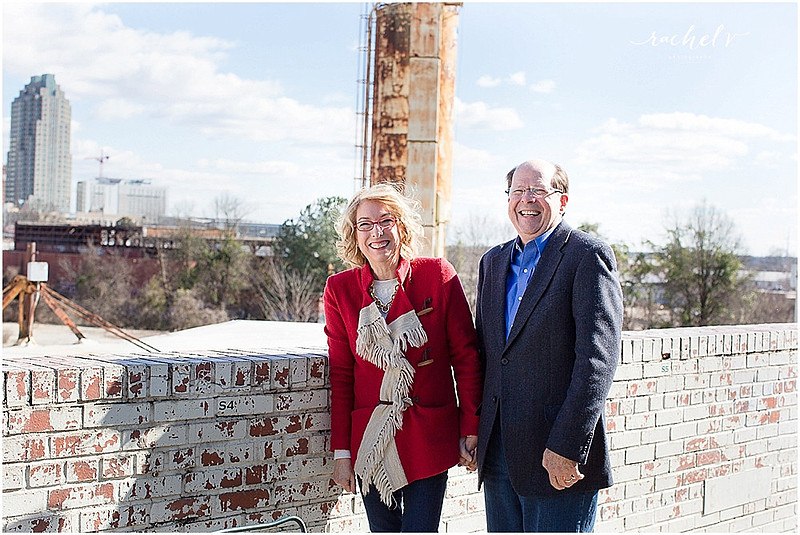 Couple standing by brick wall wearing hats and a red fringe coat with the Raleigh Sky Line