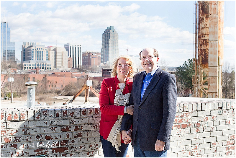 Couple standing by brick wall wearing hats and a red fringe coat with the Raleigh Sky Line